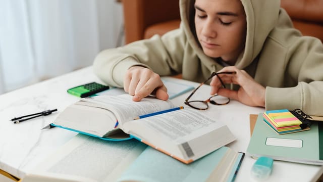 Adolescent concentré qui révise à son bureau, entouré de livres