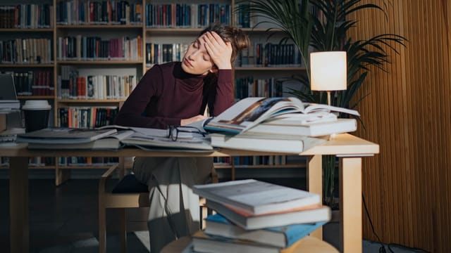 Étudiant stressé, la tête dans la main devant ses livres